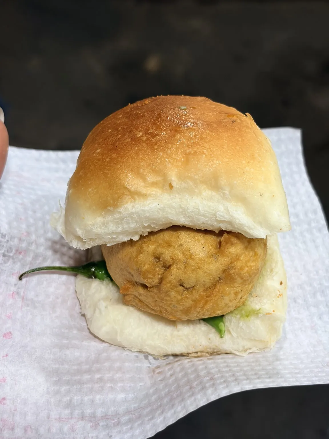 A vada pav with a green chilli, served on a paper napkin.